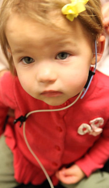 A toddler is prepared for a series of tests to ensure her hearing aids are functioning properly.